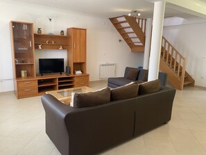Ein Wohnzimmer mit Sofa, Fernseher, Holz-Multimöbel und einer Treppe.