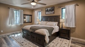 A bedroom with a bed, nightstands, a ceiling fan, and a large window with curtains. - Modern Cabin in Beautiful Pinetop (Pinetop-Lakeside)