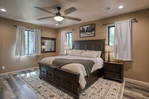 A bedroom with a bed, nightstands, a ceiling fan, and a large window with curtains. - Modern Cabin in Beautiful Pinetop (Pinetop-Lakeside)