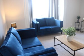 A modern living room with two blue sofas, a wooden coffee table, and a potted plant.