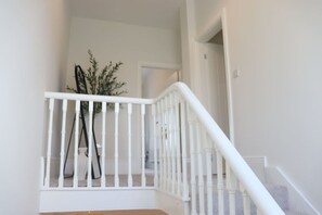 Eine weiße Treppe mit Geländer, eine Pflanze in einem schwarzen Topf und eine Tür oben.