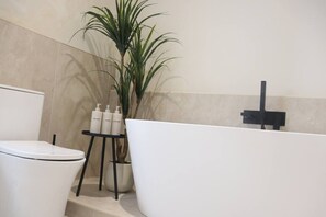 A bathroom with a white toilet, a white bathtub, and a small stand with toiletries.