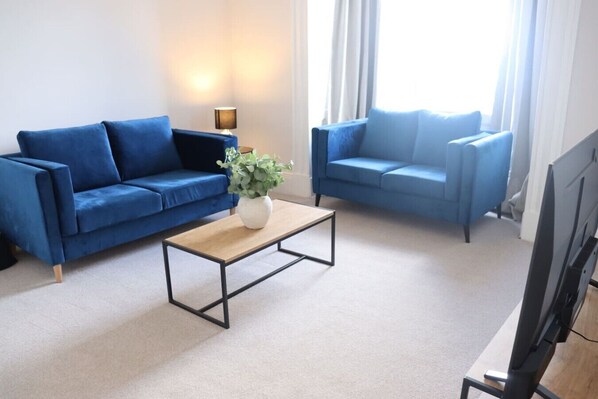A living room with two blue sofas, a coffee table, a lamp, and a TV.