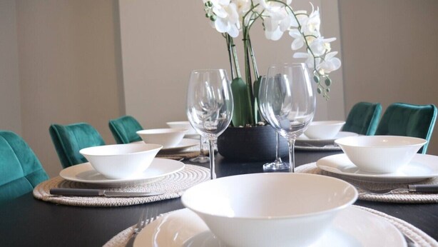 A dining table set with white bowls, wine glasses, and a potted orchid. - Seaview Terrace - 5 Bedroom seaview home (Tyne and Wear)