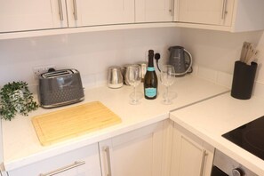 Eine Küche mit weißen Schränken, einem Toaster, einer Schneidebrett, einer Weinflasche, Gläsern, einem Wasserkocher und einem schwarzen Utensilienhalter.