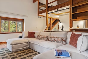 Un salon moderne avec un canapé d’angle, un escalier en bois et une grande fenêtre.