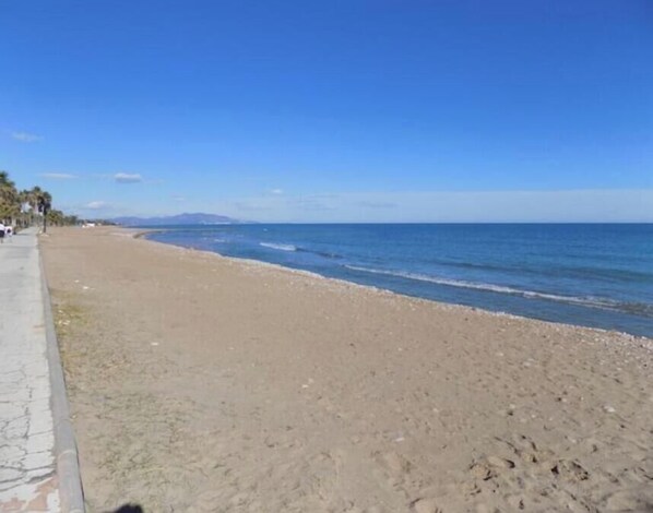 A beach with a paved walkway, calm sea, and distant mountains. - Vacances vistamar2MED005 (Castellón Comunitat Valenciana,)