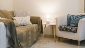 Ein Wohnzimmer mit einer Couch, einem Beistelltisch mit Lampe und einem Sessel mit Blumenkissen.