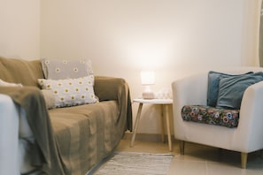 Ein Wohnzimmer mit einer Couch, einem Beistelltisch mit Lampe und einem Sessel mit Blumenkissen.