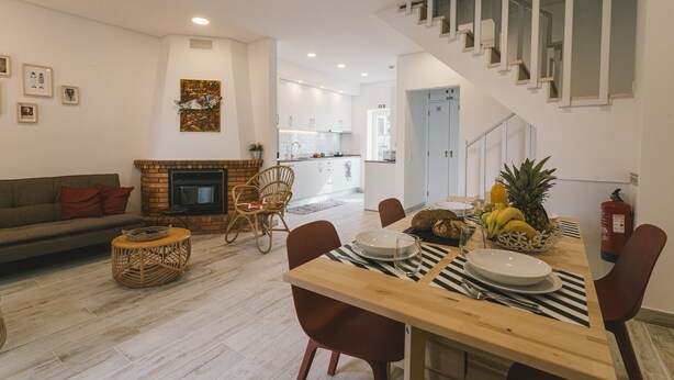 Ein modernes Wohnzimmer mit Kamin, Essbereich mit Tisch für vier Personen und einer Treppe zu einer oberen Ebene.
