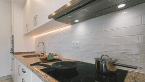 Eine moderne Küche mit weißen Schränken, einer Arbeitsplatte aus Granit, einer schwarzen Induktionskochplatte und einem Edelstahlkochtopf.
