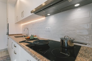 Eine moderne Küche mit weißen Schränken, einer Arbeitsplatte aus Granit, einer schwarzen Induktionskochplatte und einem Edelstahlkochtopf.