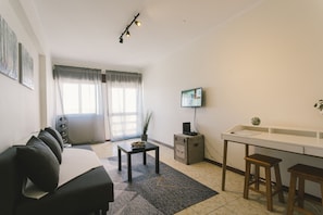 A modern living room with a sofa, a coffee table, a TV, and a desk with two stools. - Best Houses 62 - Praia da Baia Apartment (Peniche)
