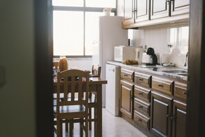 A kitchen with wooden cabinets, a white refrigerator, and a window. - Best Houses 62 - Praia da Baia Apartment (Peniche)