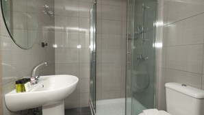 Kylpyhuone, jossa on valkoinen pesuallas, lasinen suihkuseinä ja wc-istuin.
