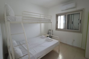 Habitación con literas, ventana, aire acondicionado y una mesita.