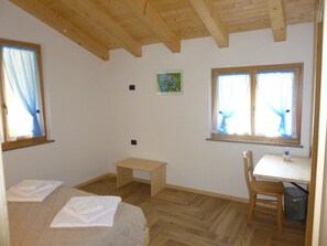 Una habitación con cama, escritorio, silla y dos ventanas con cortinas.