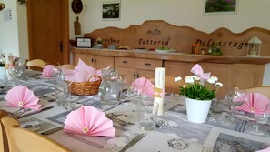 Una mesa lista para comer decorada con adornos de papel rosa, vasos transparentes y una vela blanca.