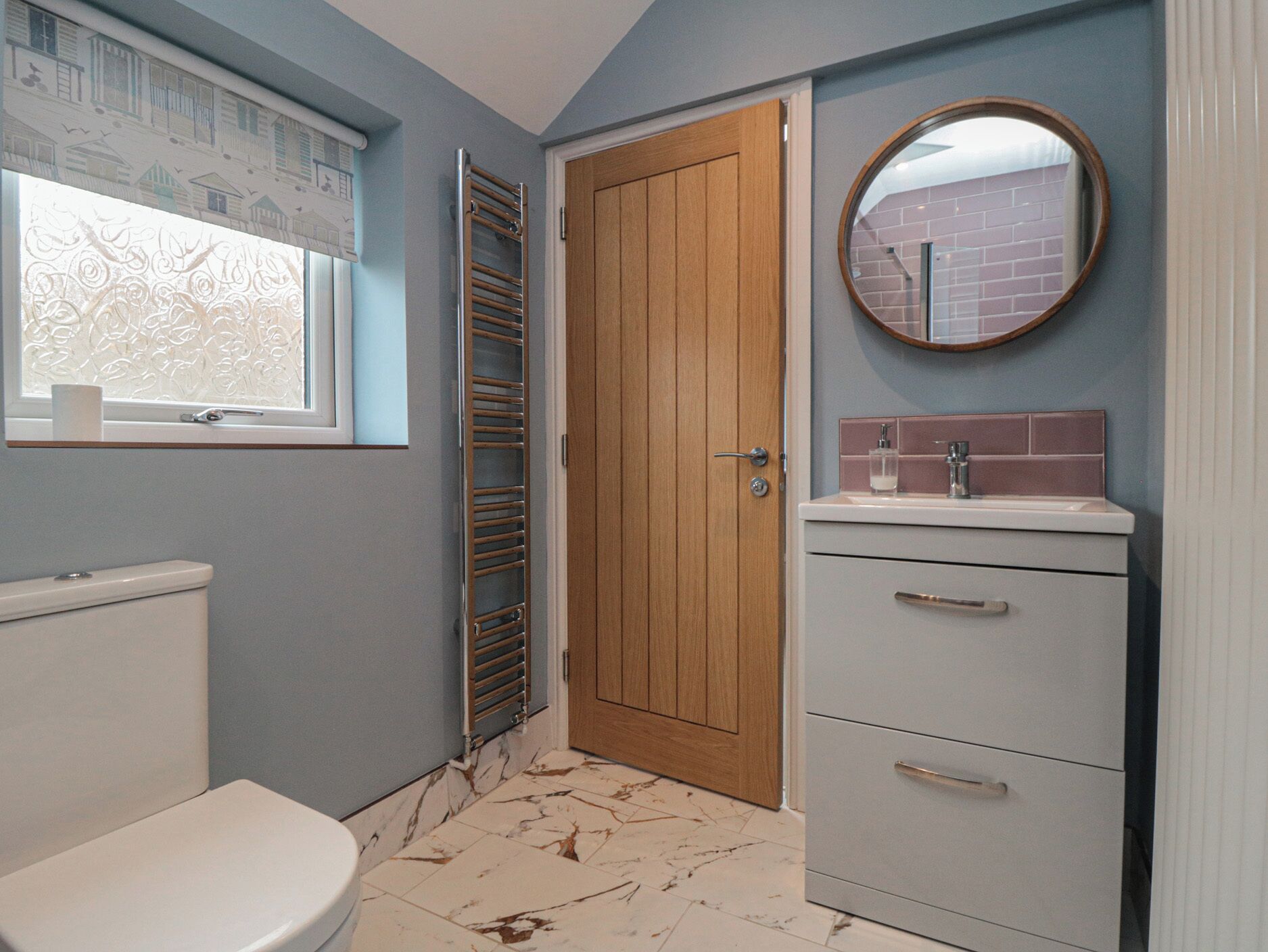 A bathroom with a toilet, a towel rack, a wooden door, a mirror, and a sink with a tiled backsplash.
