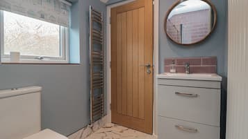 A bathroom with a toilet, a towel rack, a wooden door, a mirror, and a sink with a tiled backsplash.