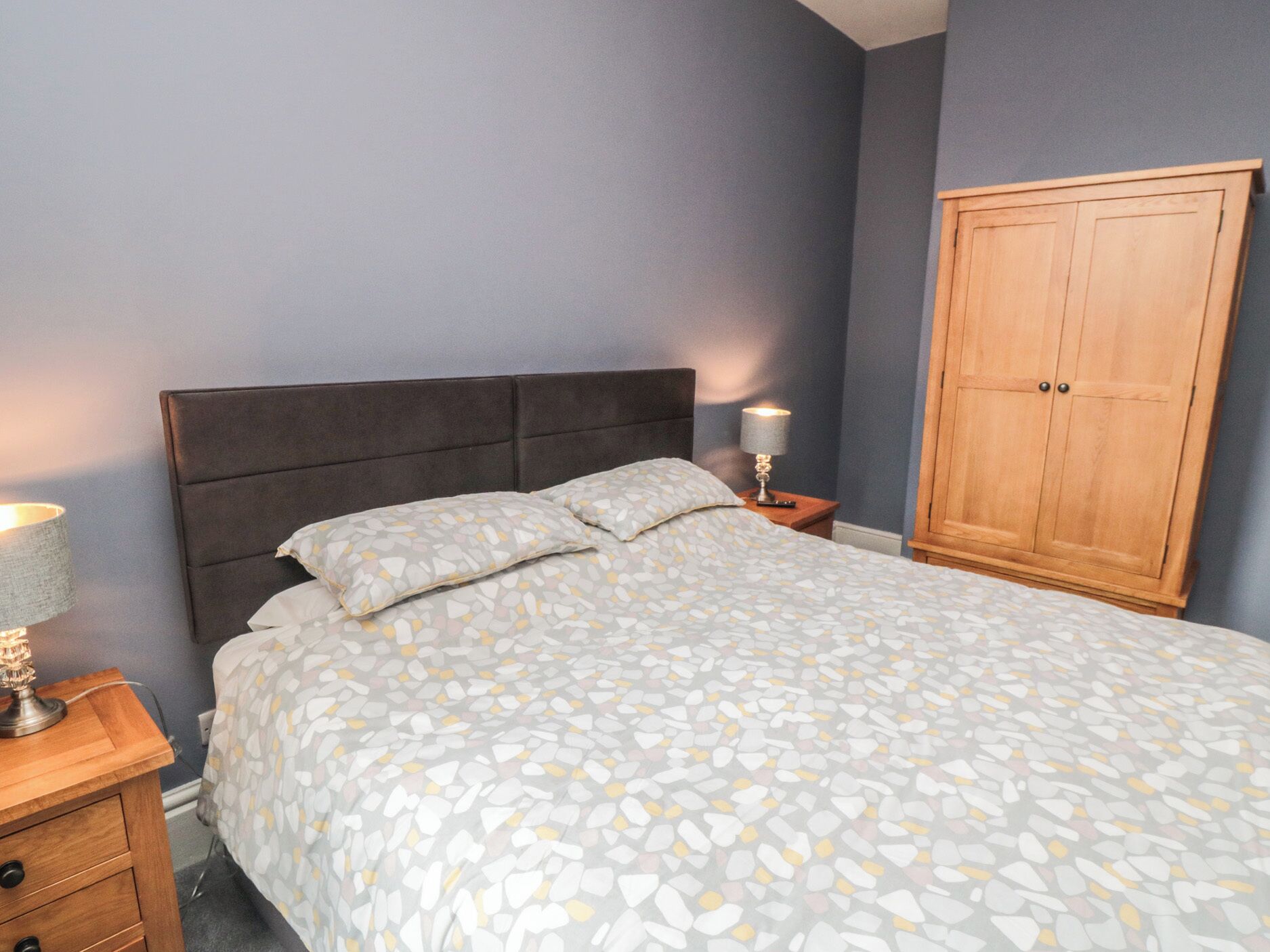 A bedroom with a bed, nightstands, a wooden wardrobe, and a lamp.