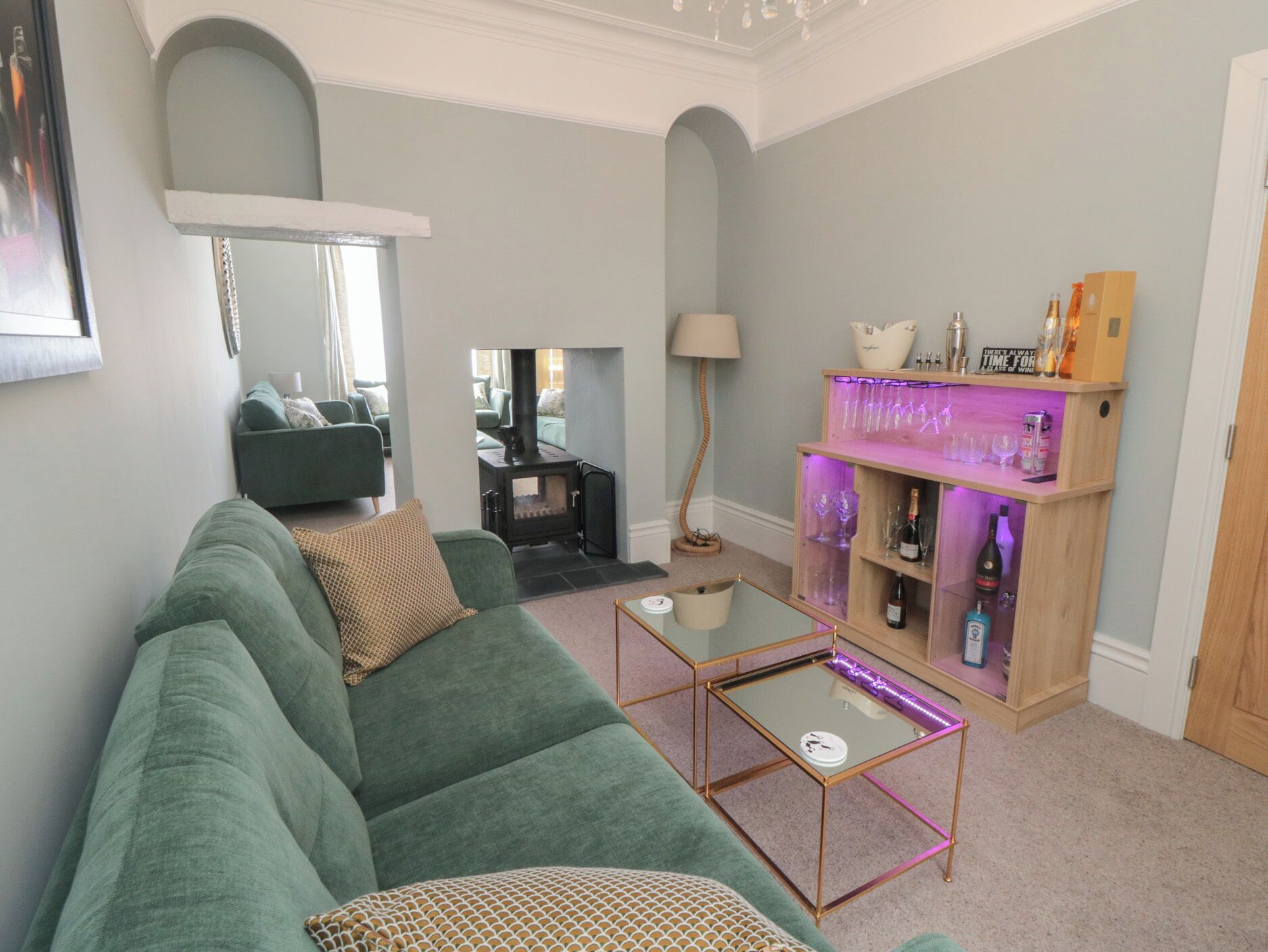 Ein Wohnzimmer mit einem grünen Sofa, einem Glastisch, einem Kamin und einer Bar mit Flaschen.