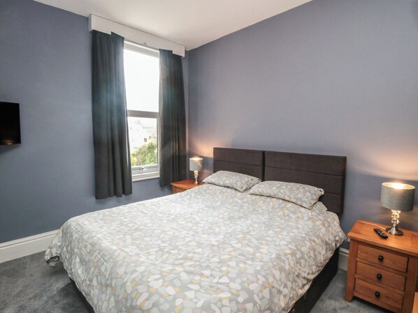 A bedroom with a bed, a nightstand, a lamp, and a window with curtains.