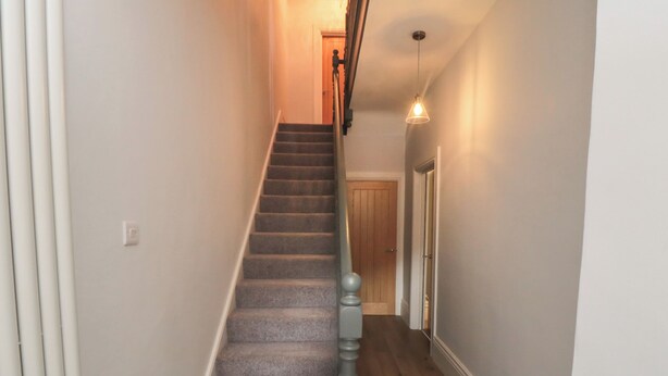 A staircase with carpeted steps, a wooden handrail, and a light fixture above. - Ruby's Retreat (Filey)