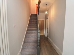 A staircase with carpeted steps, a wooden handrail, and a light fixture above.