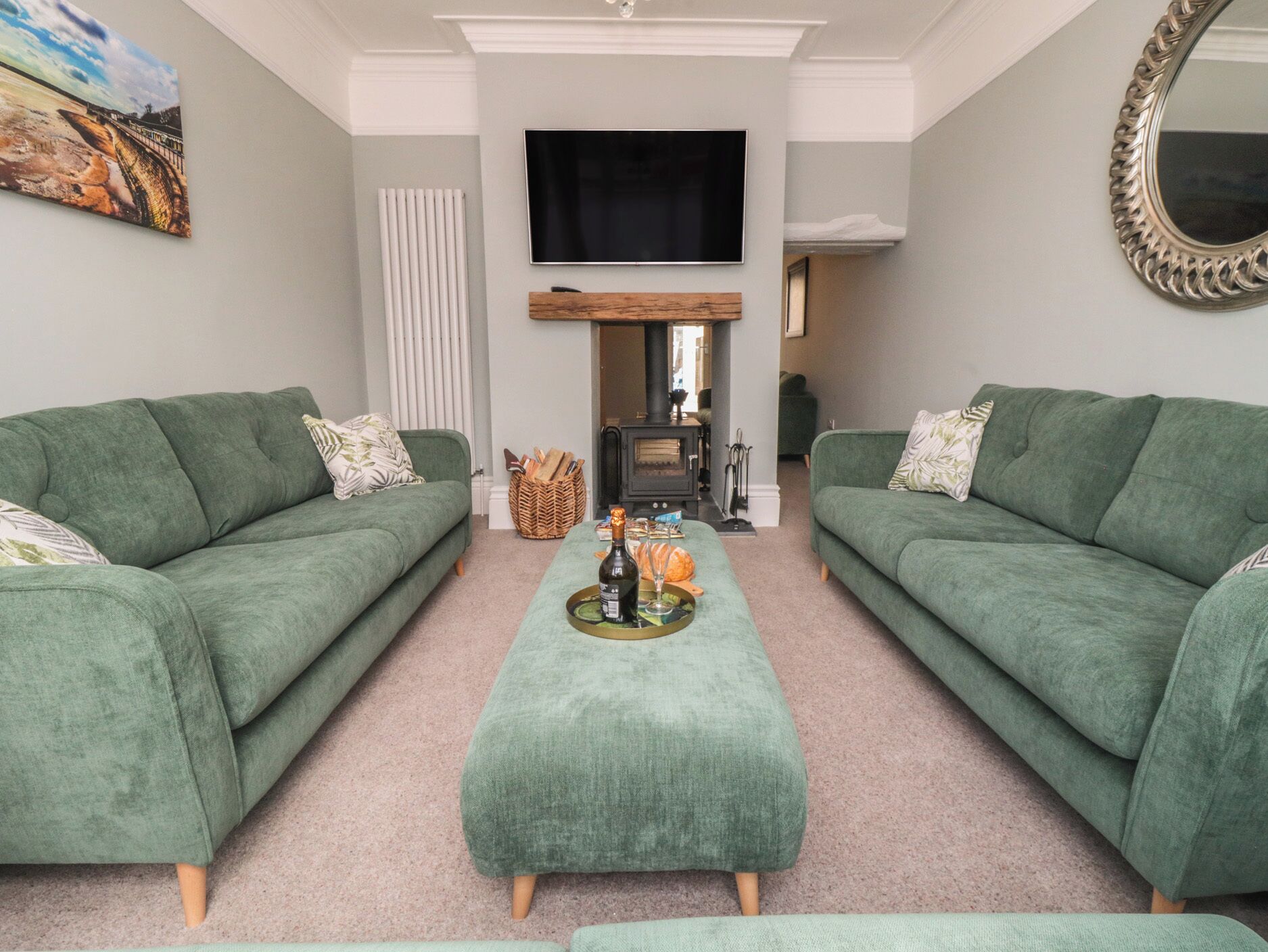 A living room with two green sofas, a central ottoman, a fireplace, a television, and a painting on the wall.