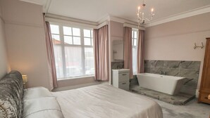 A bedroom with a large bed, a bathroom with a bathtub, and a window with curtains. - Ruby's Retreat (Filey)