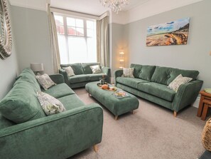 A living room with green sofas, a coffee table, a lamp, and a painting on the wall.