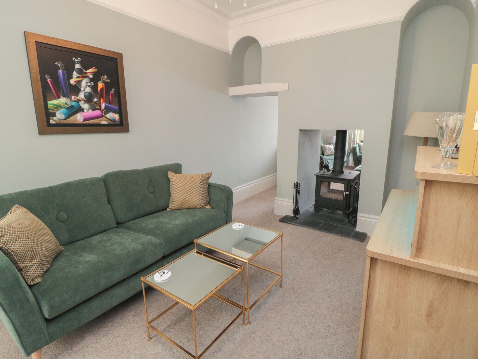 A living room with a green sofa, a glass-top coffee table, a fireplace, and a painting on the wall.