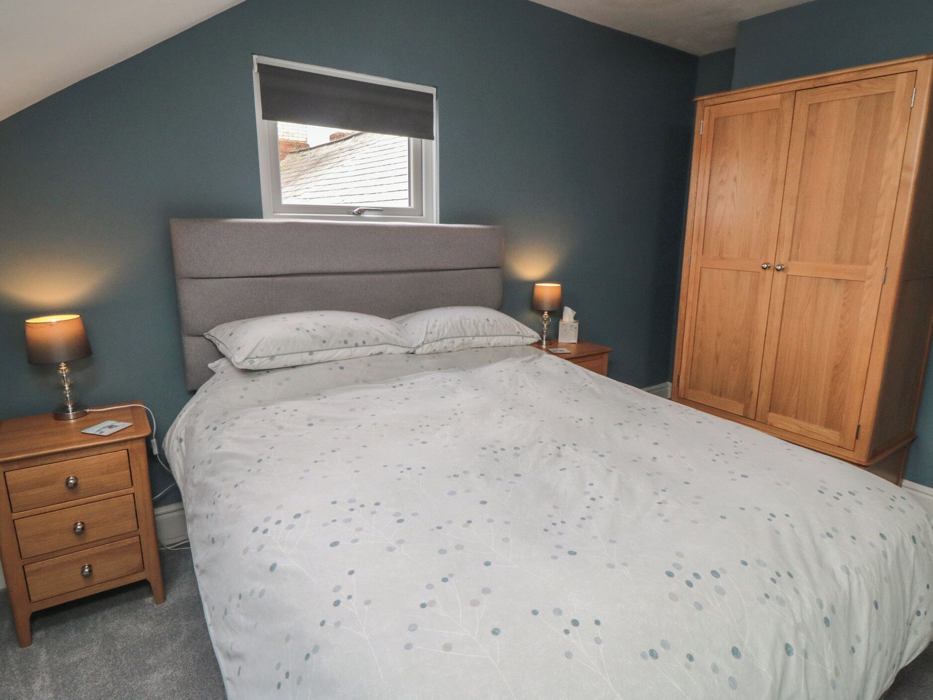 Een slaapkamer met een bed, twee nachtkastjes, een kledingkast en een raam met een blind.