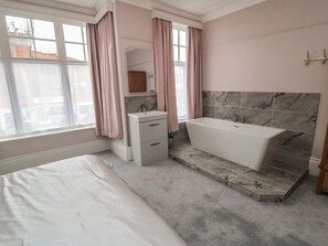A bedroom with a bed, a small bedside table, a mirror, and a window with curtains.