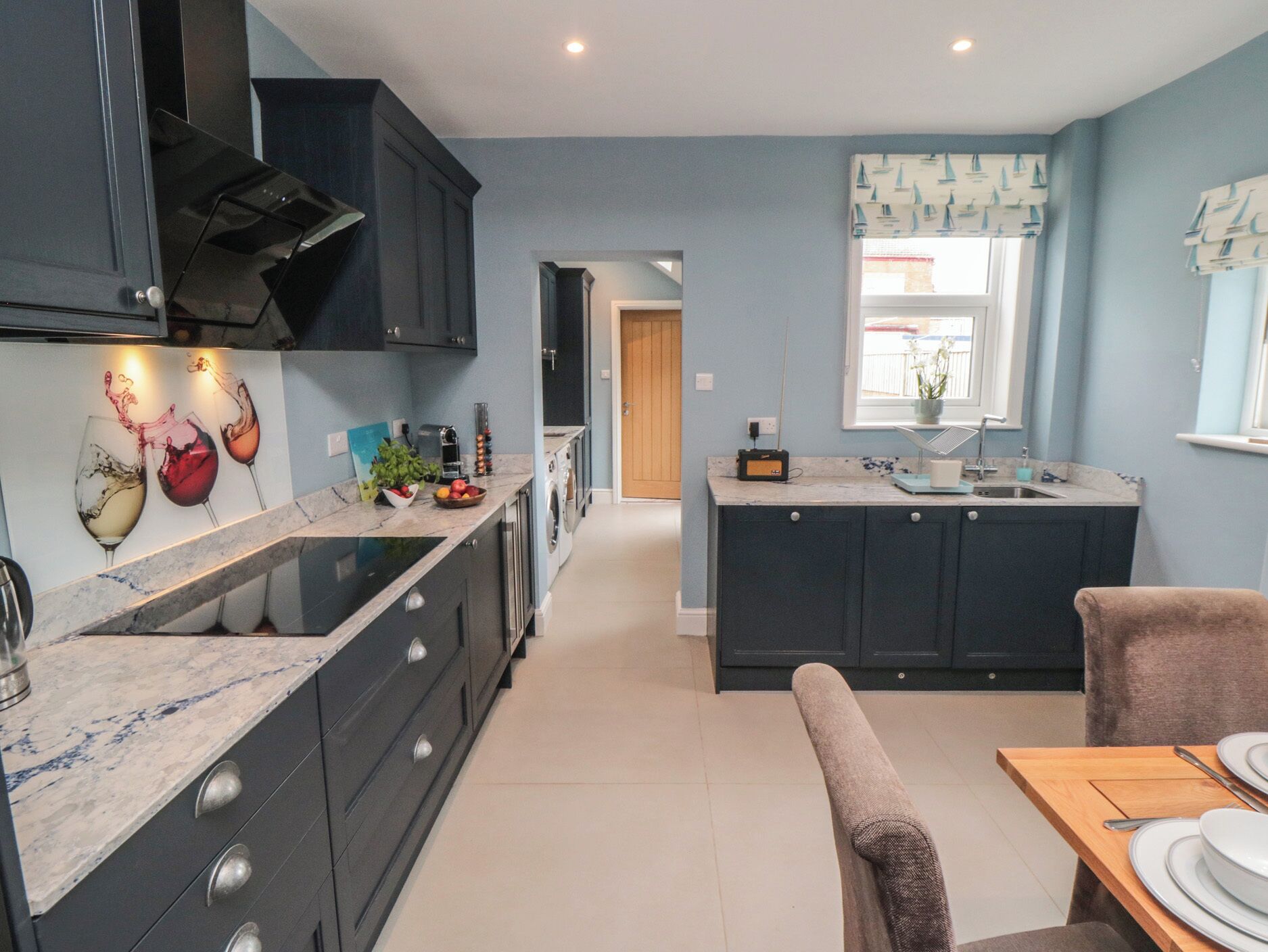 A modern kitchen with dark cabinetry, a marble countertop, and a dining area with a wooden table and chairs.