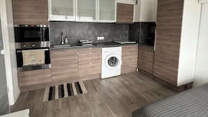 Een kleine keuken met een wasmachine, inbouwoven en kastjes.