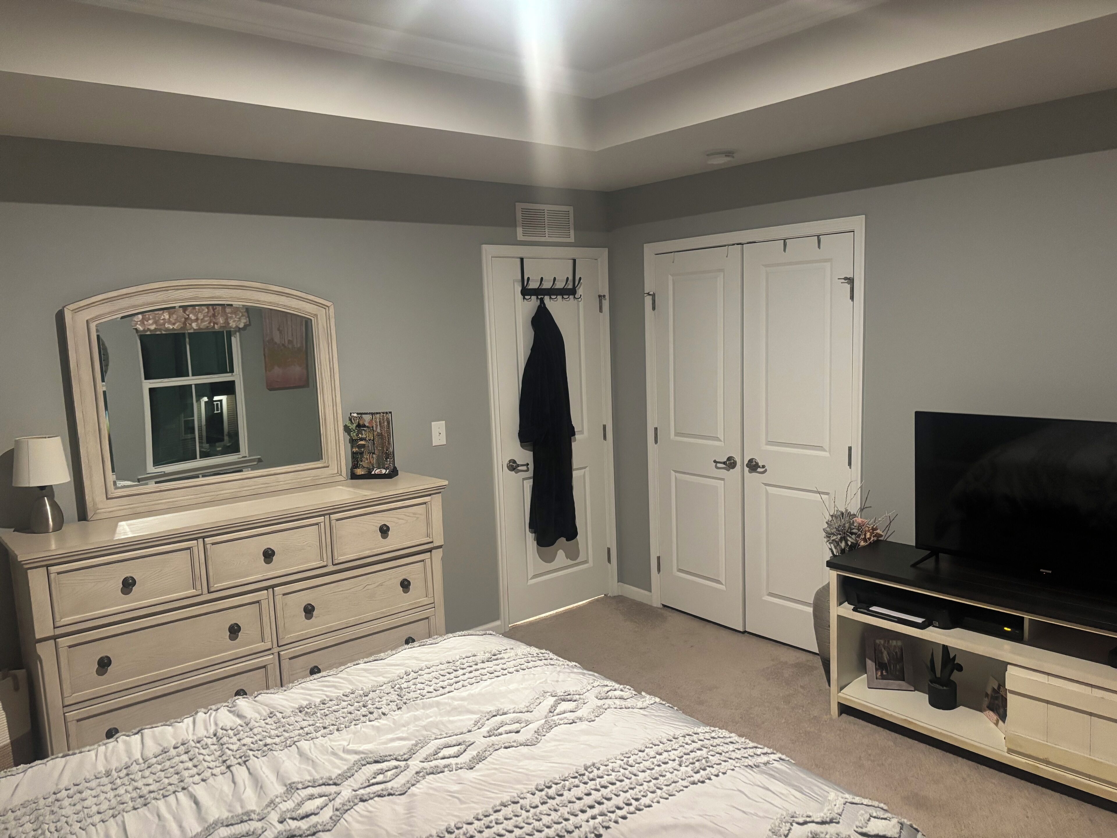 Een slaapkamer met een bed, een dressoir, een televisie en twee deuren.