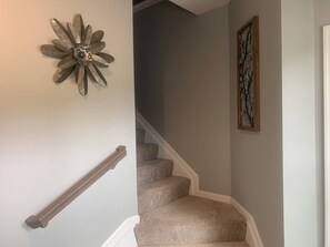Eine Treppe mit Teppichstufen, einem Holzgeländer, einer Wanddekoration mit Blumen und einem gerahmten Kunstwerk.