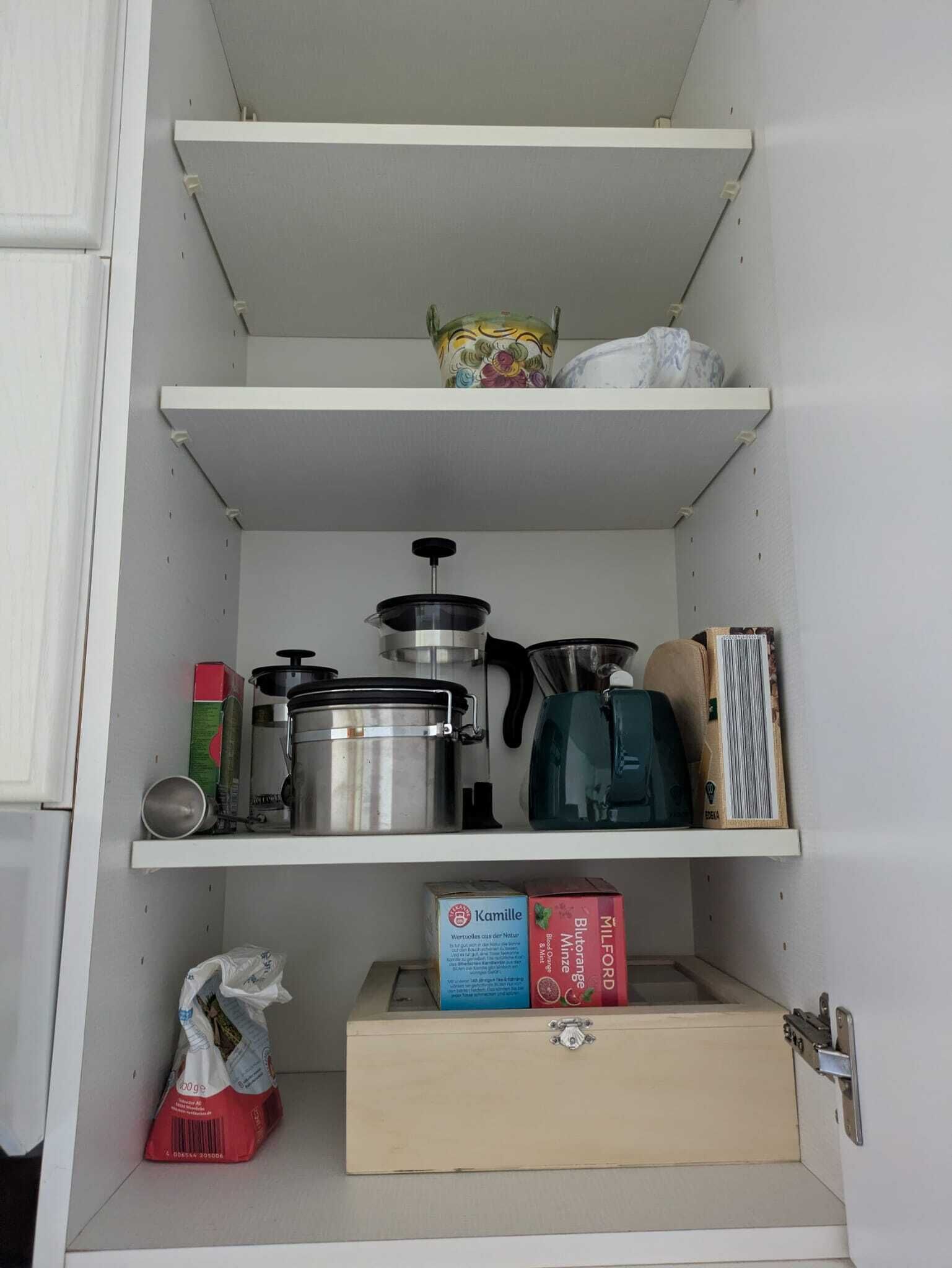 A kitchen pantry with shelves, a pot, a coffee maker, and a box of Kamille tea.