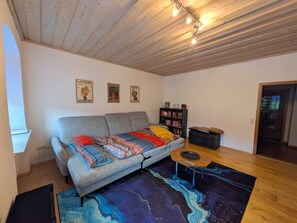 A cozy living room with a gray sofa, a bookshelf, a wooden ceiling, and a patterned rug. - Spacious apartment | 4-6 persons | 5 min to Bayernpark (Reisbach)