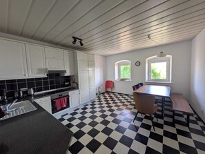 Keittiössä on valkoiset kaapit, mustavalkoruutukuviollinen lattia, punainen tuoli ja ikkuna, josta avautuu näkymä vehreään maisemaan.
