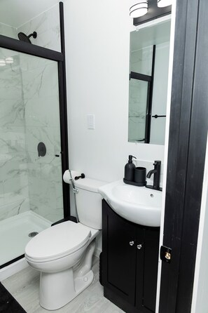 A bathroom with a white toilet, a black sink, a glass shower enclosure, and a mirror above the sink.