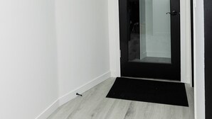 Un couloir avec une porte à cadre noir, des murs blancs et un plancher en bois clair.