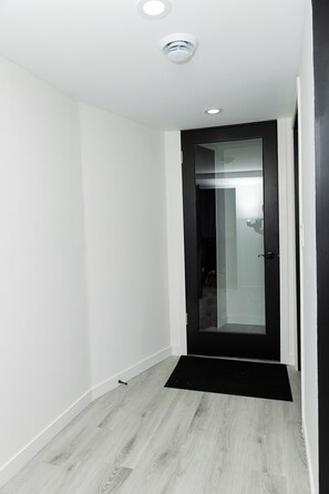 Un couloir avec une porte à cadre noir, des murs blancs et un plancher en bois clair.