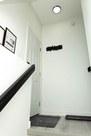 Uma escadaria com uma porta branca no topo, um objeto preto fixado na parede e um tapete na base.