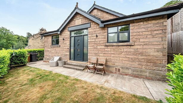A stone house with a dark front door, two windows, and a small porch with outdoor seating. - Stunning Retreat in Matlock Bath (Matlock)
