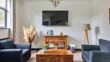 A modern living room with a large flat-screen TV, a wooden coffee table, two sofas, a floor lamp, and a painting on the wall.