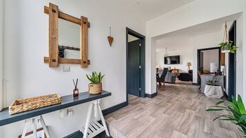 Una sala de estar moderna con piso de madera oscura, un espejo grande, una consola negra con una cesta tejida y una escalera blanca.