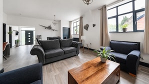 A modern living room with a grey sofa, a wooden coffee table, and a large window with curtains. - Stunning Retreat in Matlock Bath (Matlock)